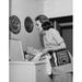 Side profile of a young woman putting clothes into a washing machine Poster Print (24 x 36)